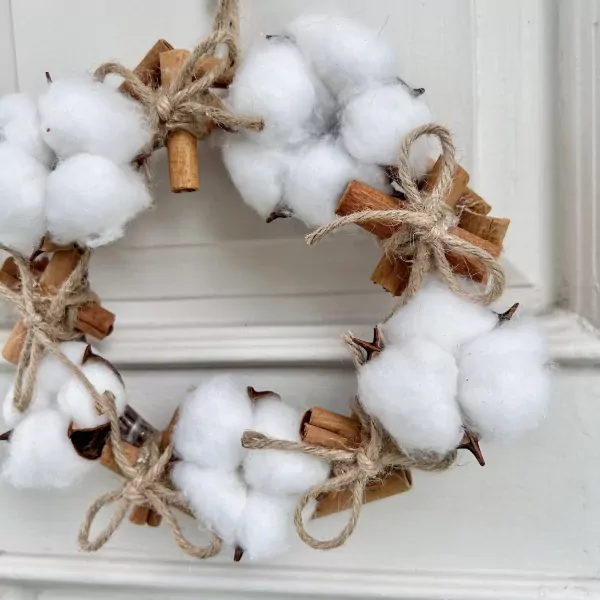 Cotton Flower Mistletoe wreath with cinnamon sticks and twine on a white background.