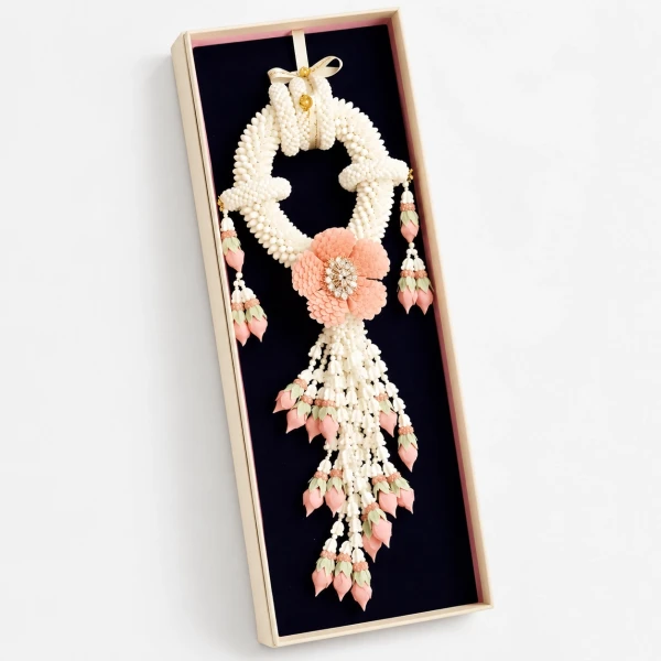 Ornate white and pink jasmine garland with a large pink flower, displayed in a dark box.
