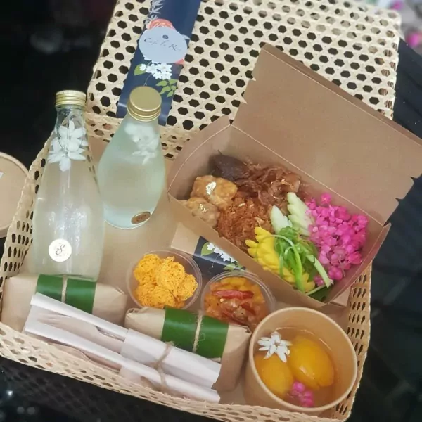 Khao Chae set with rice, bottles of jasmine water, mangoes, and various savory side dishes in a woven basket.