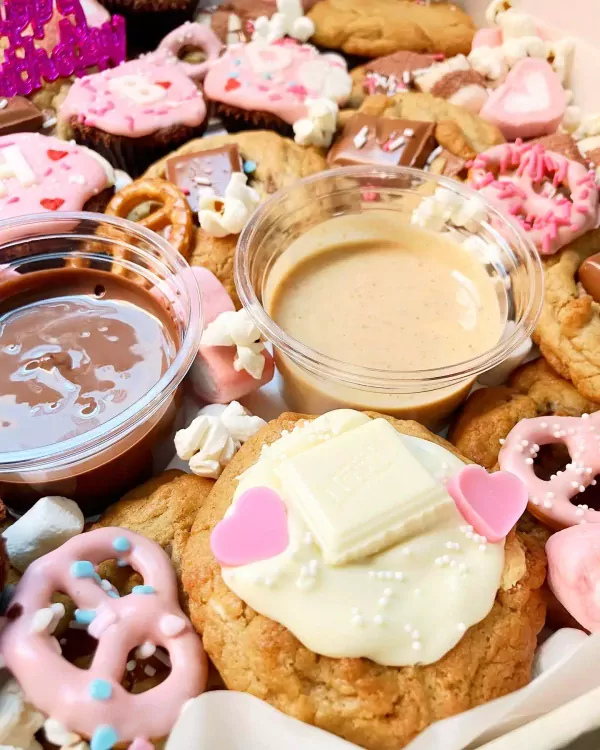 A dessert box filled with cookies, brownies, and dips, decorated with hearts and sprinkles.