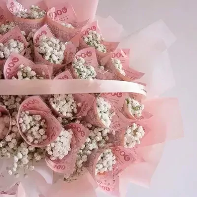Money bouquet with pink banknotes rolled into cones filled with tiny white flowers.