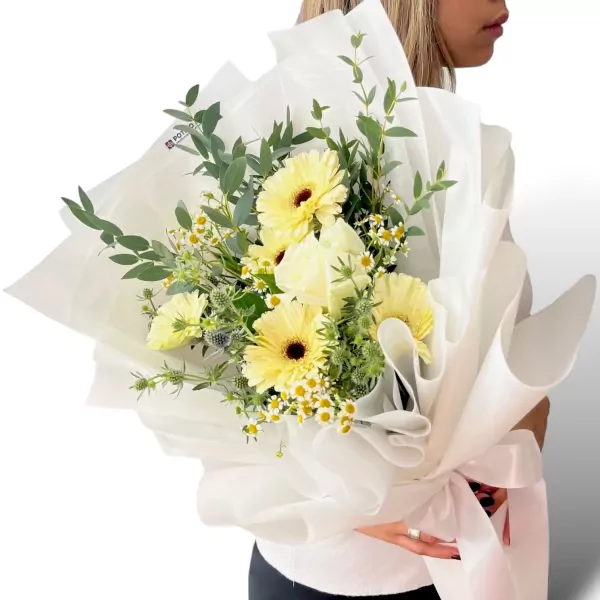 A bouquet of white gerbera daisies and roses wrapped in white paper and tied with a white ribbon.