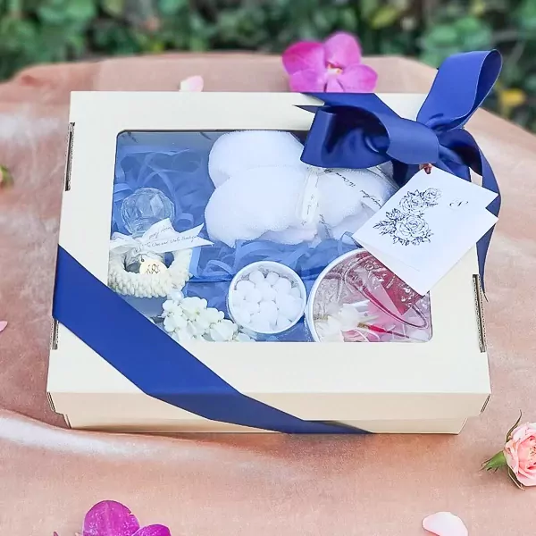 Thai Water Ceremony Set M gift box with white fluffy items, white flower garland, small white candies, and a perfume bottle.