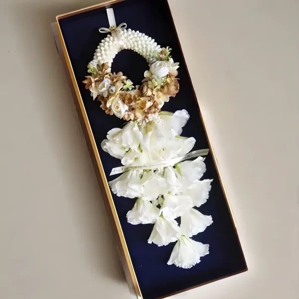 An artificial white and gold floral garland in an acrylic box, with white flowers cascading down.
