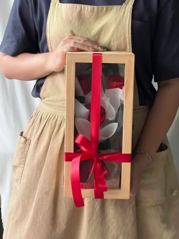 Wooden box with three preserved red and white roses, tied with a red ribbon.