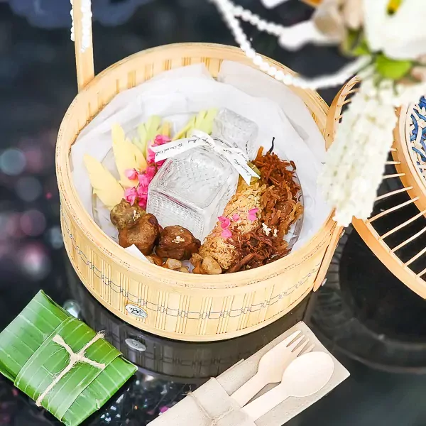 Bamboo basket filled with Thai Khao Chae dishes, bottle, and utensils.