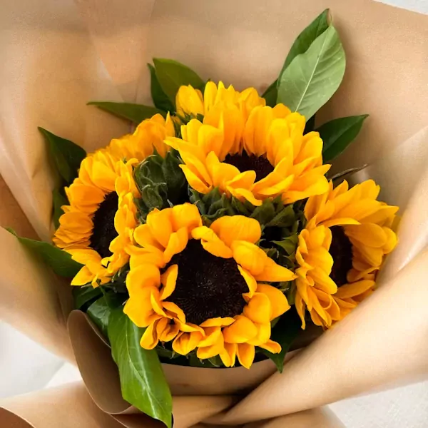 A bouquet of bright yellow sunflowers wrapped in brown paper.