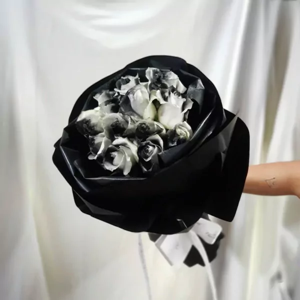 Bouquet of black and white roses wrapped in black paper, held by a person with a tattoo on their arm.