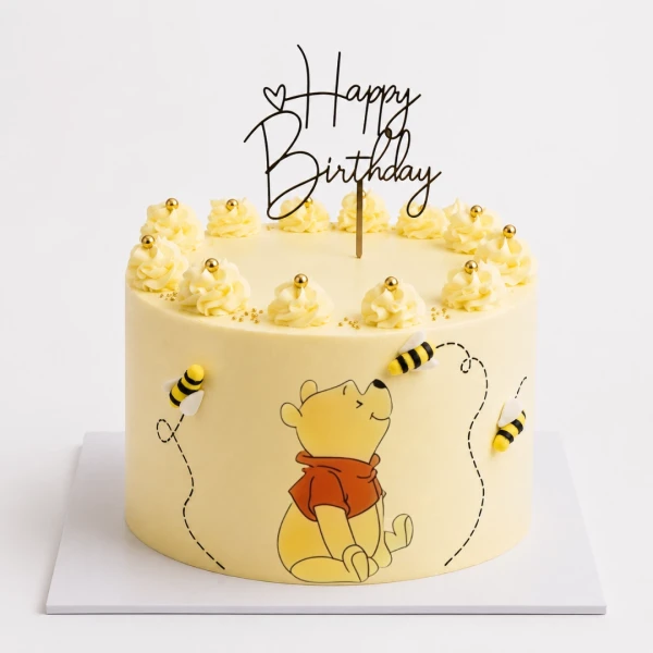 Winnie the Pooh cake with bees and "Happy Birthday" topper, decorated with yellow frosting swirls.