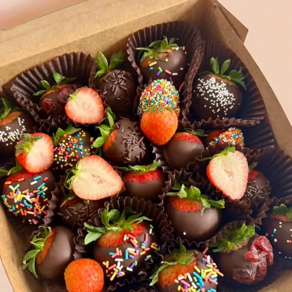 Box of chocolate-dipped strawberries with sprinkles and some sliced in half.