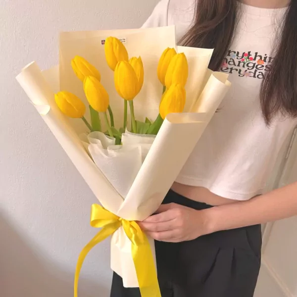A bouquet of 10 yellow tulips wrapped in yellow and cream paper, tied with a yellow ribbon.