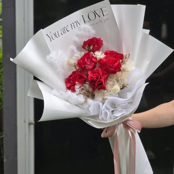 Red roses and white dried flowers in a bouquet with a "You are my LOVE" note.