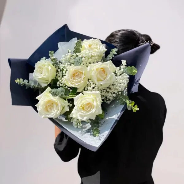 White roses with baby's breath and eucalyptus in navy blue wrapping paper.