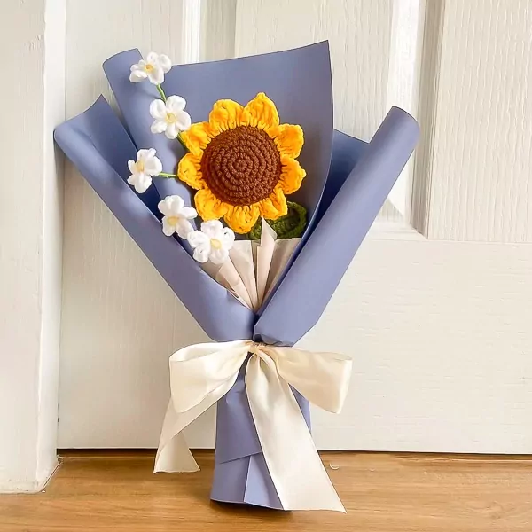 Crocheted sunflower bouquet in blue paper wrap with white flowers and ivory ribbon.