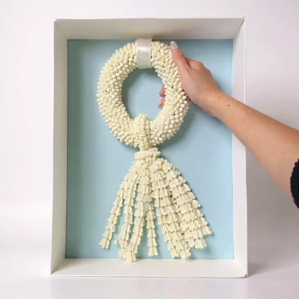 A hand holding a white jasmine garland in a light blue box.
