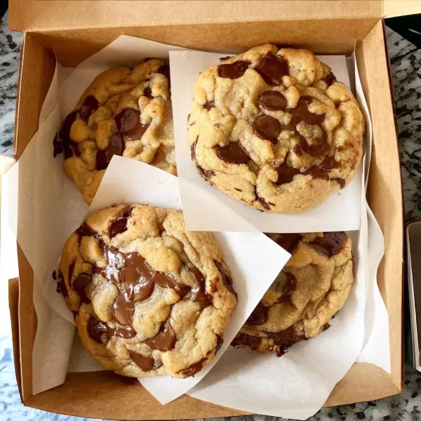 Box of four large, golden brown chocolate chip cookies, with gooey, melted chocolate chunks.