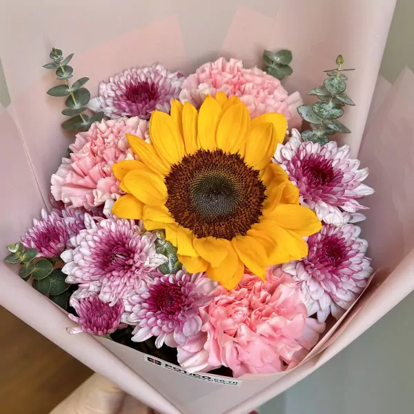 Bouquet of a large sunflower surrounded by pink carnations and purple-pink chrysanthemums.