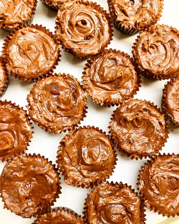 Chocolate fudge brownie bites with frosting swirls in brown wrappers.