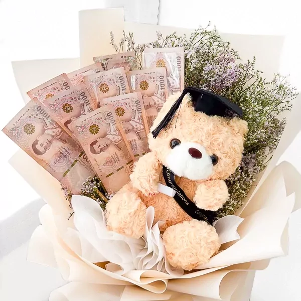 A graduation teddy bear with a cap and gown in a bouquet with Thai baht banknotes.