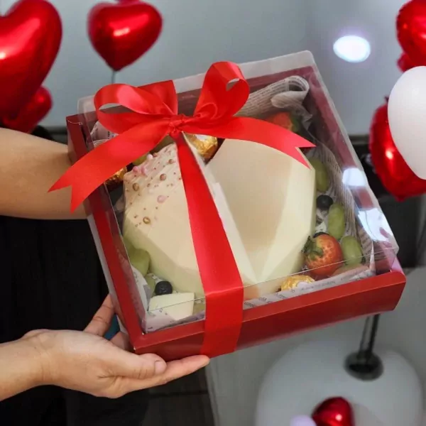 White heart-shaped chocolate cake with fruits and Ferrero Rochers in a red gift box.