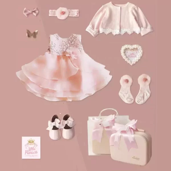 Pink baby gift set with dress, shoes, socks, headband, jacket, and suitcase.