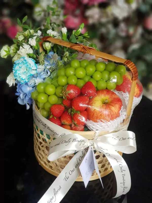 Fruit basket with grapes, strawberries, apples, and blue and white flowers in a woven basket.