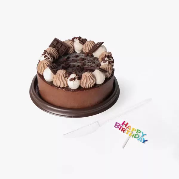 Chocolate cake with whipped cream, chocolate shavings, and chocolate bars, with a "Happy Birthday" topper.