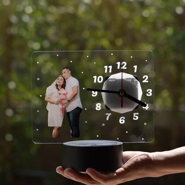 Couple's photo on a clear acrylic clock with LED base, held in a hand.