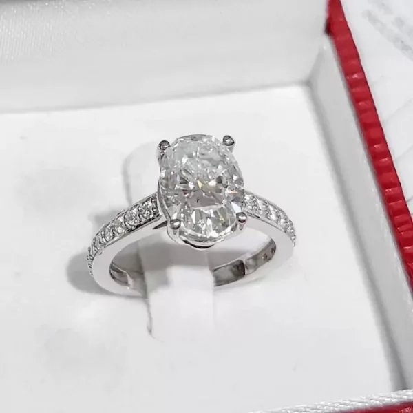 Oval-cut moissanite diamond ring with pavé band in a jewelry box.