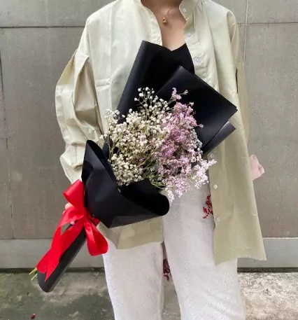 Woman holding a bouquet of white and pink dried limonium flowers, wrapped in black paper and tied with a red bow.