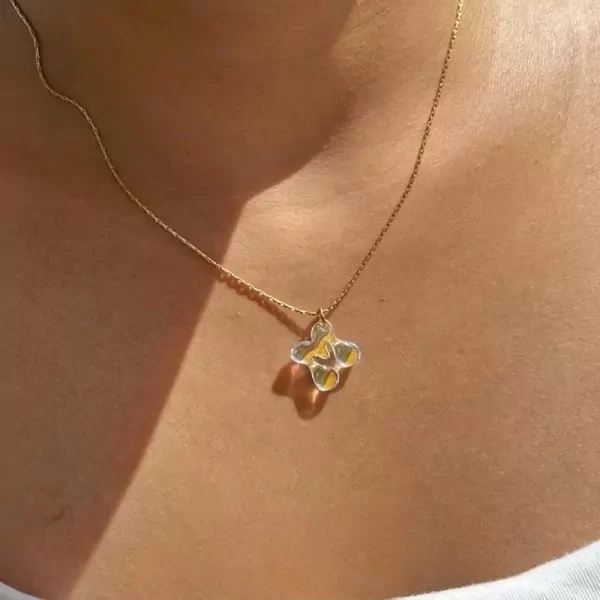 Close-up of a gold necklace with a translucent, four-leaf clover-shaped pendant with yellow accents.