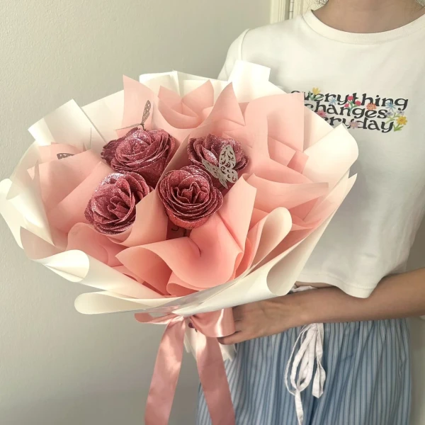 Woman holding a bouquet of glittery pink roses with a white and pink wrapper, tied with a pink ribbon.