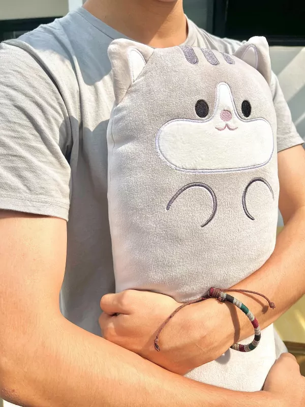 Person holding a large, grey, plush cat pillow with embroidered face and arms.