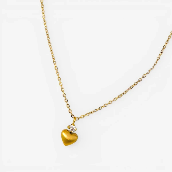 Gold chain necklace with a heart pendant accented by a small crystal.
