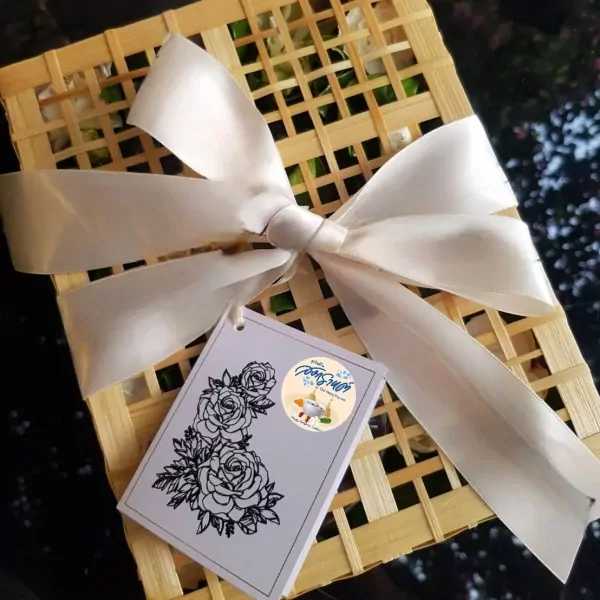 A woven box tied with a cream ribbon, holding fresh flowers and a tag with roses.