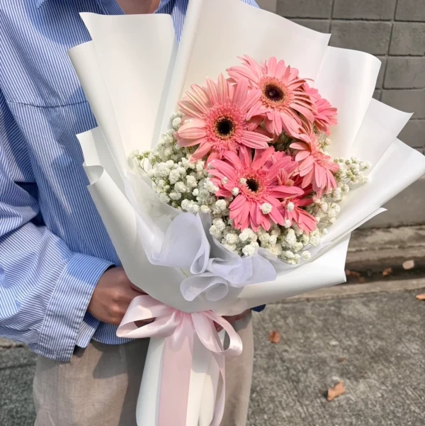 Pink gerbera daisies and baby's breath bouquet wrapped in white paper and tied with a pink ribbon.