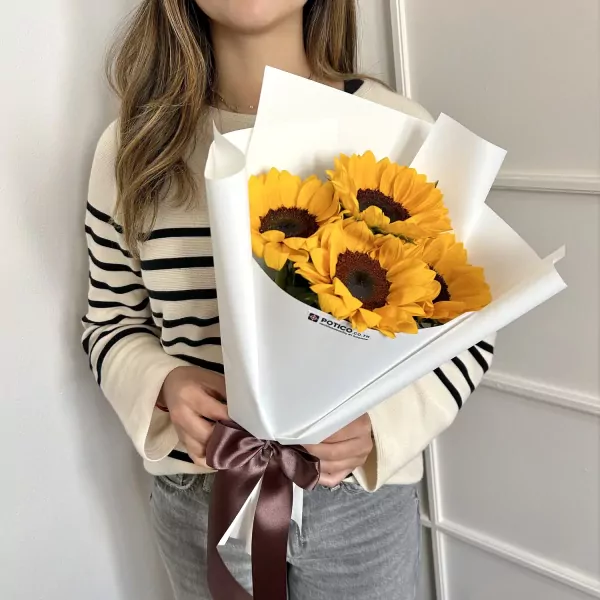 Woman in striped sweater holding bouquet of sunflowers wrapped in white paper, tied with a brown ribbon.