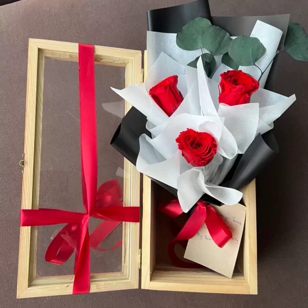 Wooden box with a bouquet of red roses and eucalyptus, tied with red ribbons.