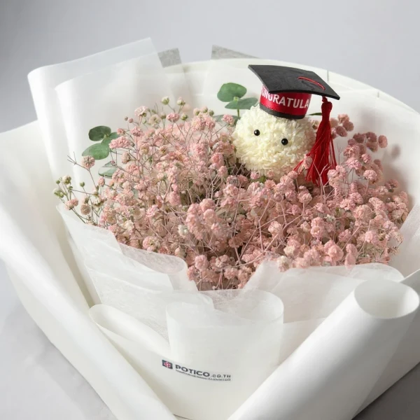 A graduation bouquet with a teddy bear wearing a cap, surrounded by pink baby's breath flowers.