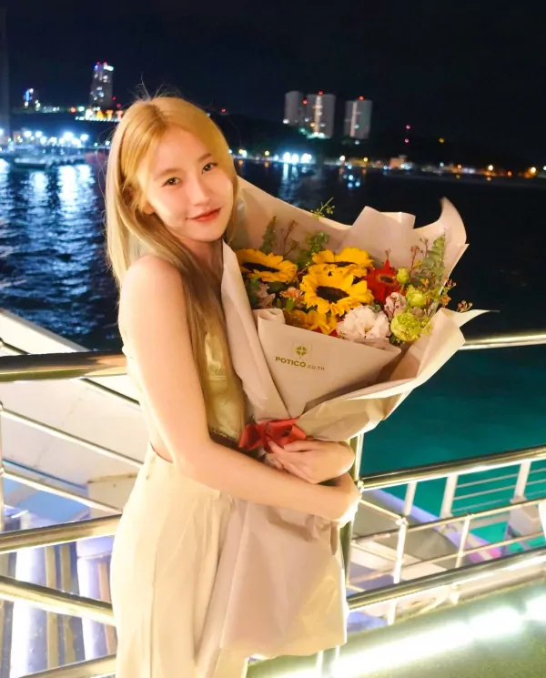 Woman holding a sunflower bouquet on a balcony at night with city lights in the background.
