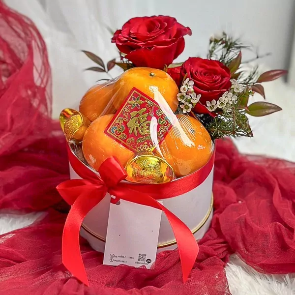 Chinese New Year oranges in a white box with red ribbon, roses, and gold decorations.