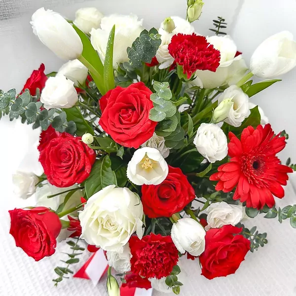 Red and white roses, tulips, gerbera, and carnations in a floral arrangement with eucalyptus.