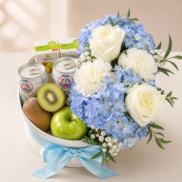 A gift box with fruit, milk, juice, and a bouquet of white roses and blue hydrangeas.