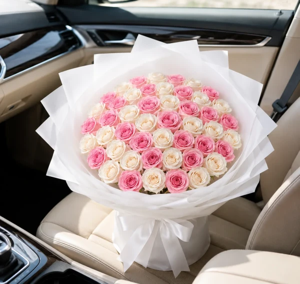 Bouquet of 50 pink and white roses, arranged in a white paper wrapper, resting on a car seat.