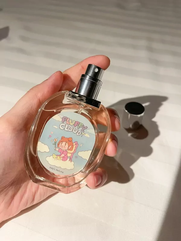 Hand holding a "Fluffy Cloud" perfume bottle with a cartoon girl on the label.