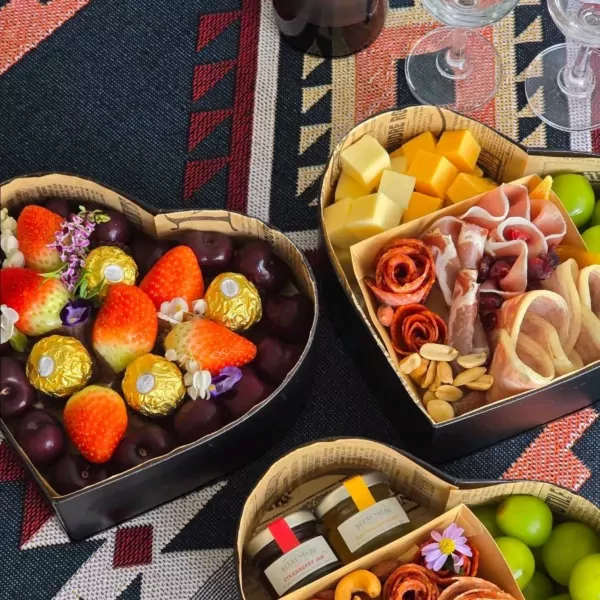 Heart-shaped box overflowing with strawberries, cherries, and golden chocolates.