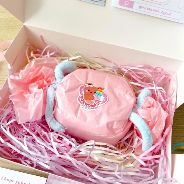 Candle set in a gift box with pink tissue paper and shredded filler, featuring a pink wrapped candle with a bear sticker.