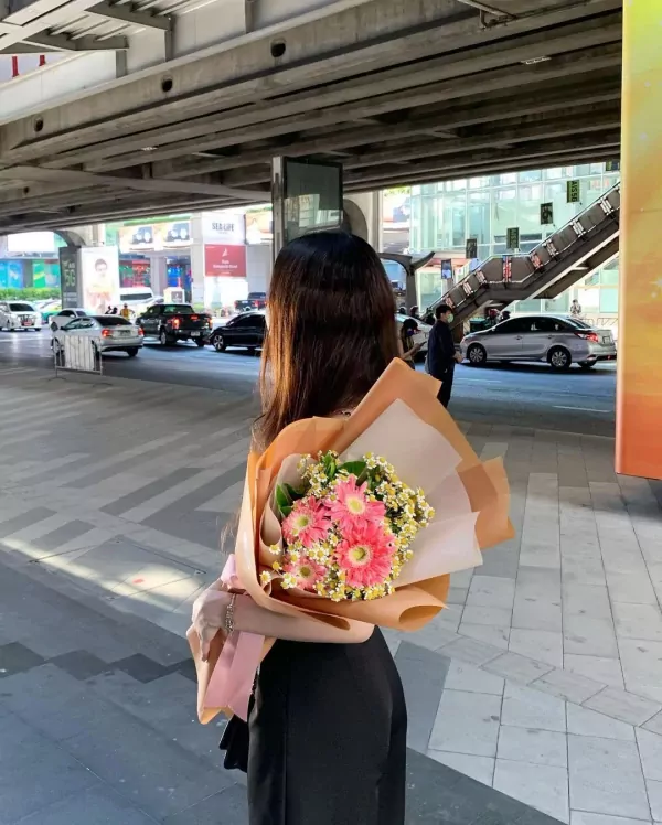 Woman holding a bouquet of pink gerbera daisies and white daisies.