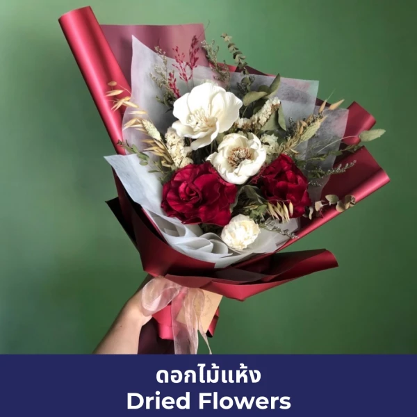 Hand holding a bouquet of dried white and red flowers with red wrapping.
