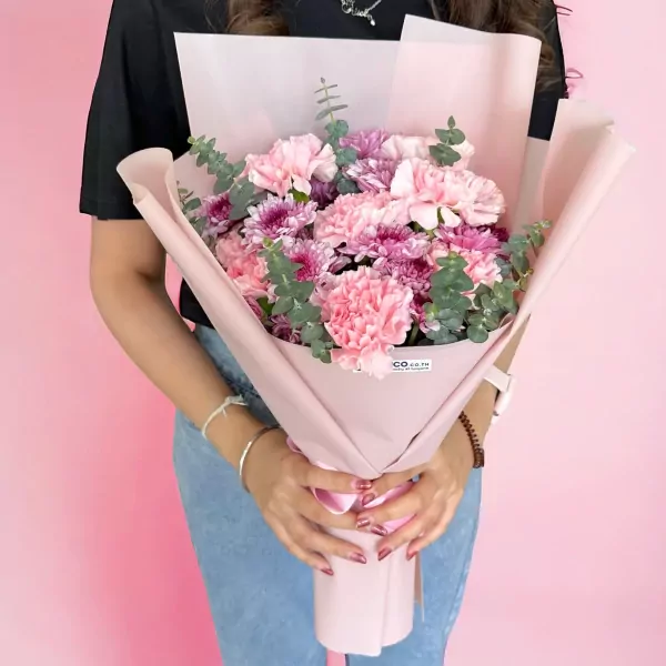 Bouquet of pink carnations and purple mums wrapped in pink paper, held by a person.